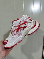 Side view of a white and red ASICS sneaker showing the layered mesh upper, overlays, laces, and sculpted outsole.