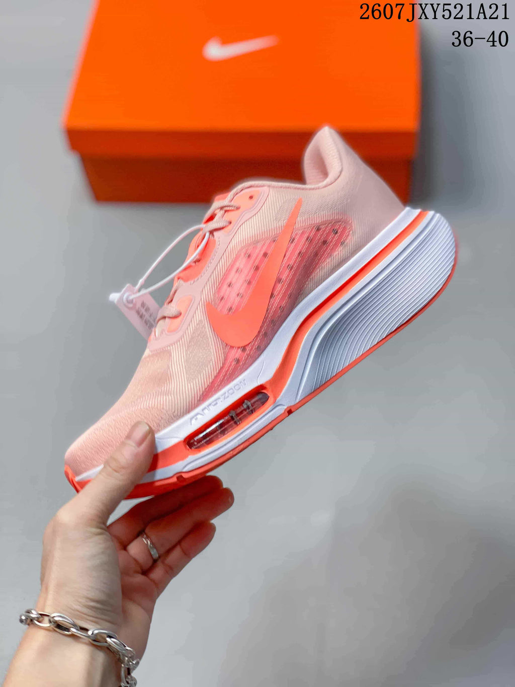 Side view of a pale pink and coral Nike sneaker showing the layered upper, side swoosh, white midsole, and visible Air Zoom detail.
