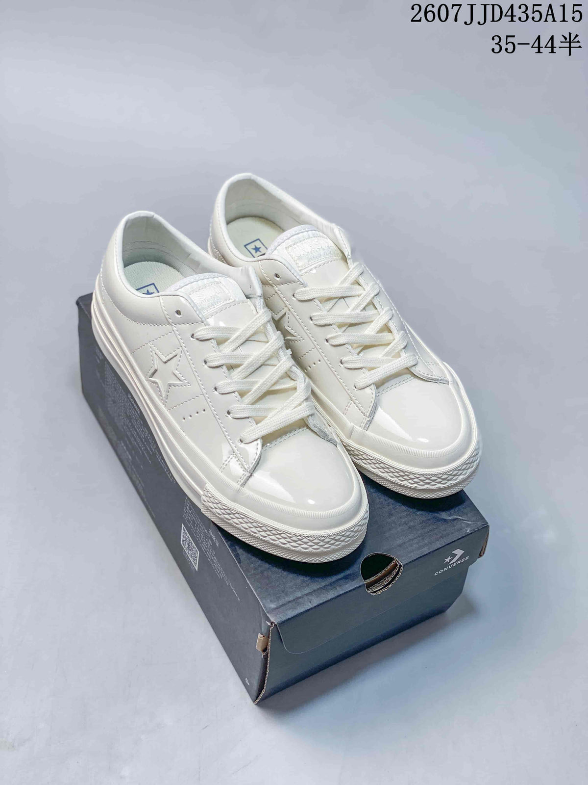 Pair of white Converse One Star J sneakers displayed on a Converse shoebox.