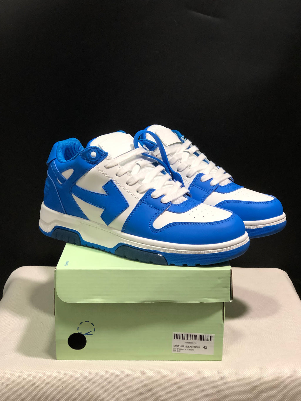 Pair of blue and white low-top sneakers displayed on a green shoebox.