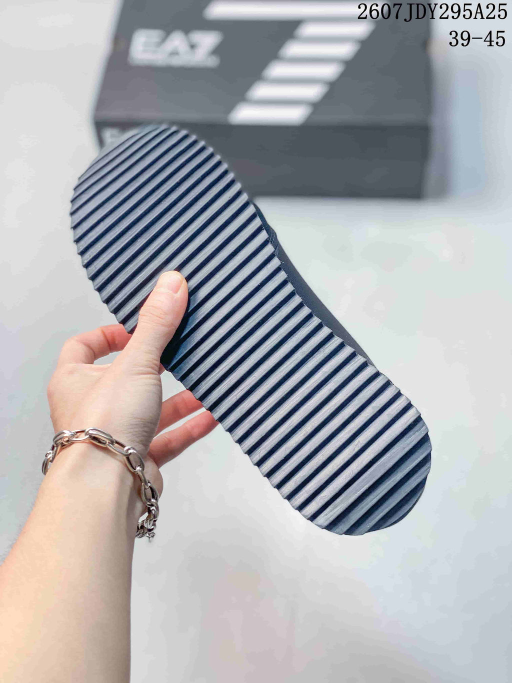 Close-up of the sneaker outsole showing a repeating diagonal tread pattern; the shoebox in the background displays EA7 branding.