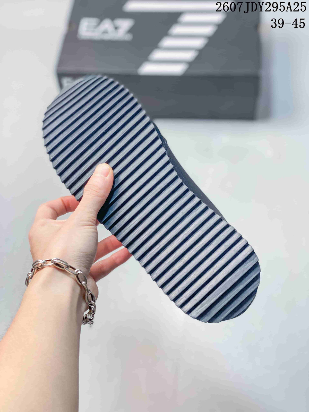 Close-up of the sneaker outsole showing a repeating diagonal tread pattern; the shoebox in the background displays EA7 branding.