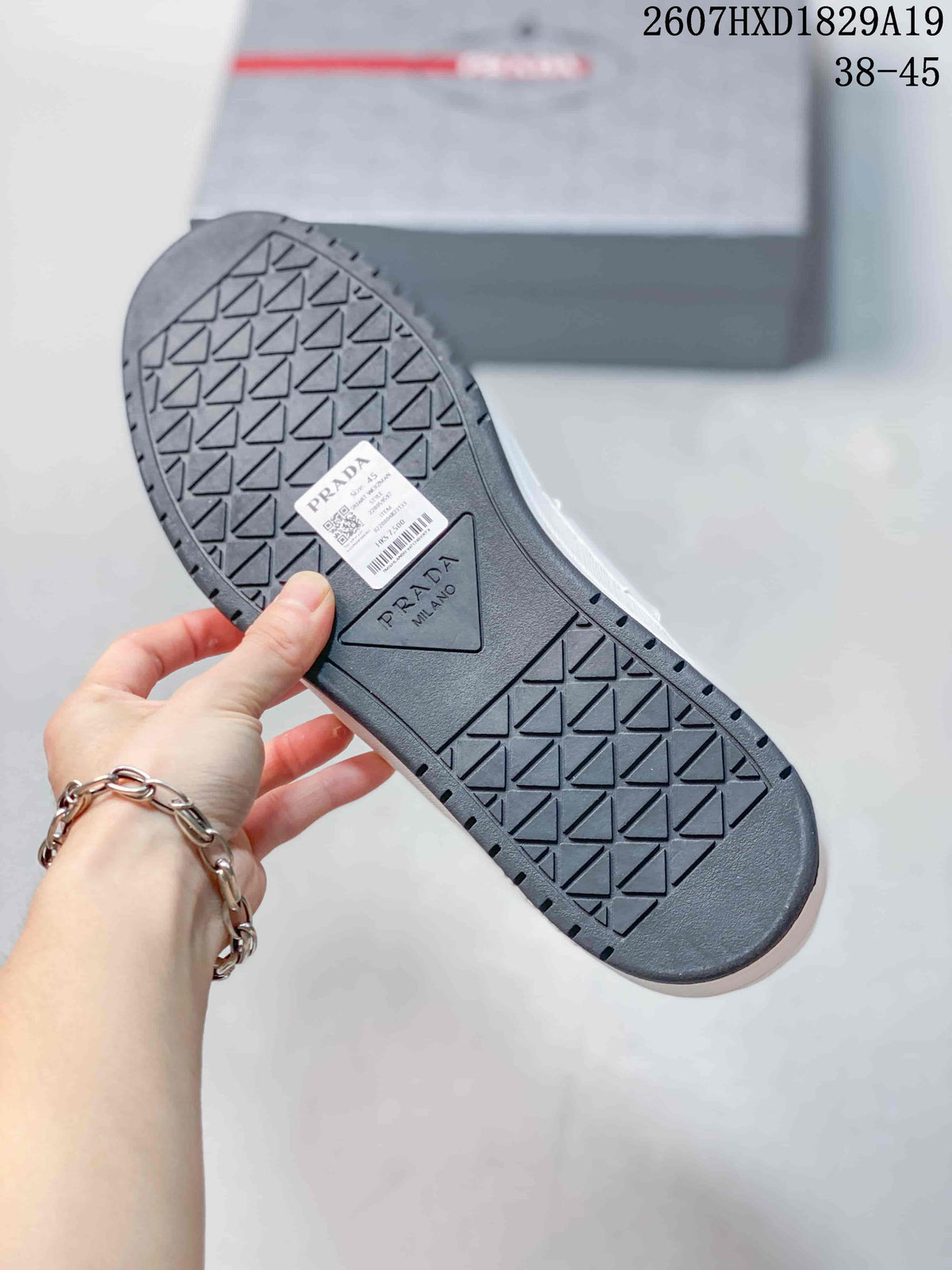 Close view of the sneaker outsole showing geometric tread and a Prada Milano panel, with a product label attached.