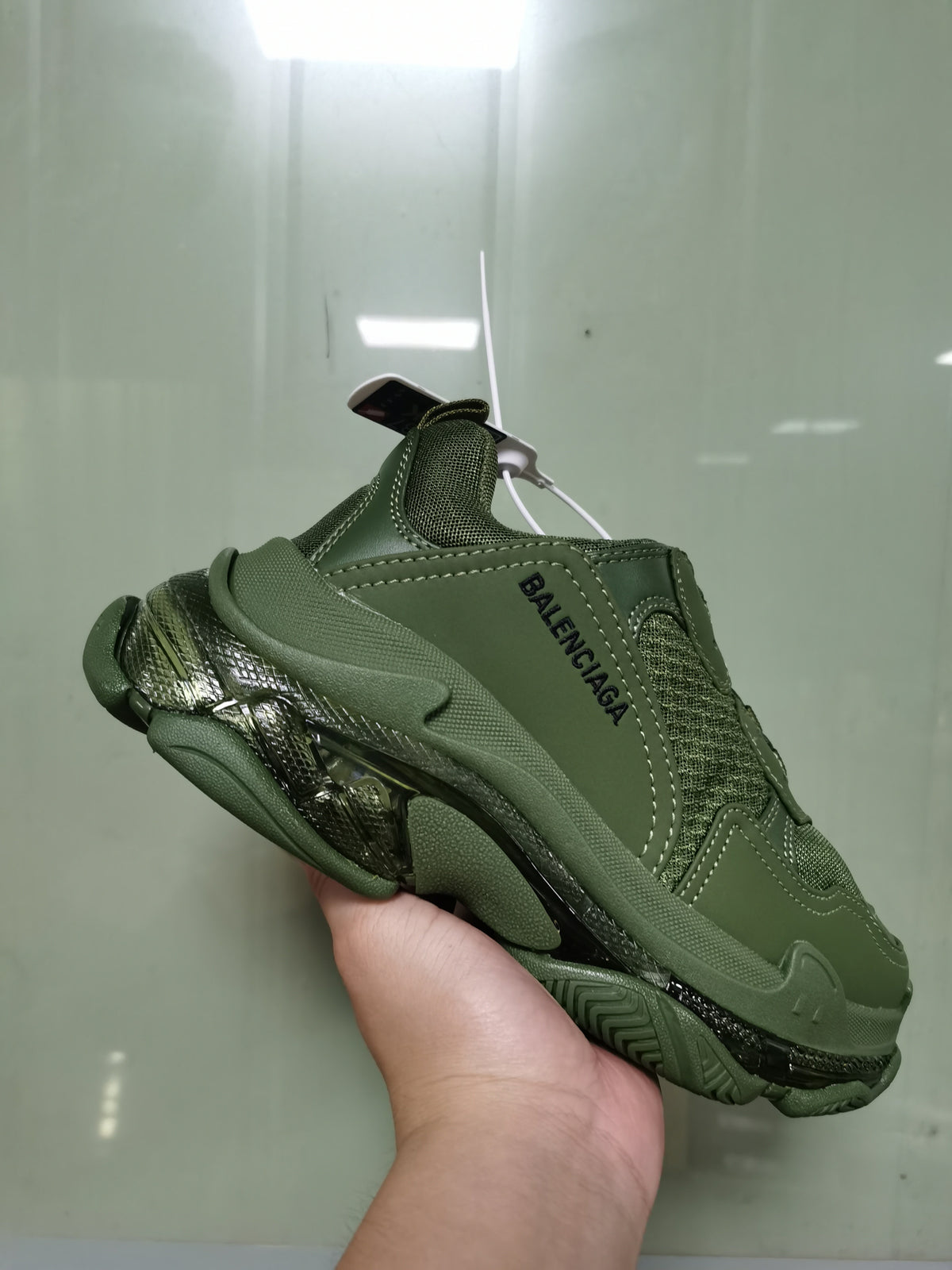 Side view of an army green Balenciaga Triple S sneaker showing mesh panels, tonal stitching, black branding and a chunky layered sole.