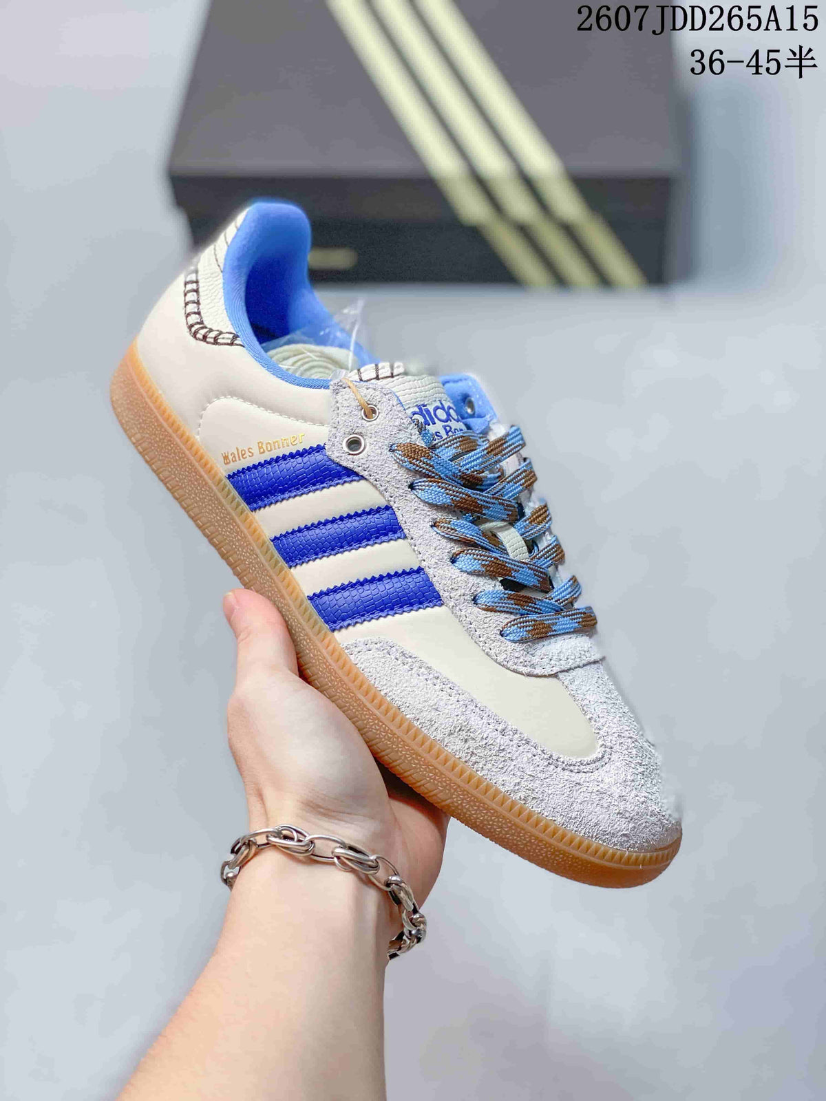 Close side view of a white and blue adidas Samba sneaker showing blue three-stripe detailing, textured toe area, patterned laces, and a gum-colored sole.
