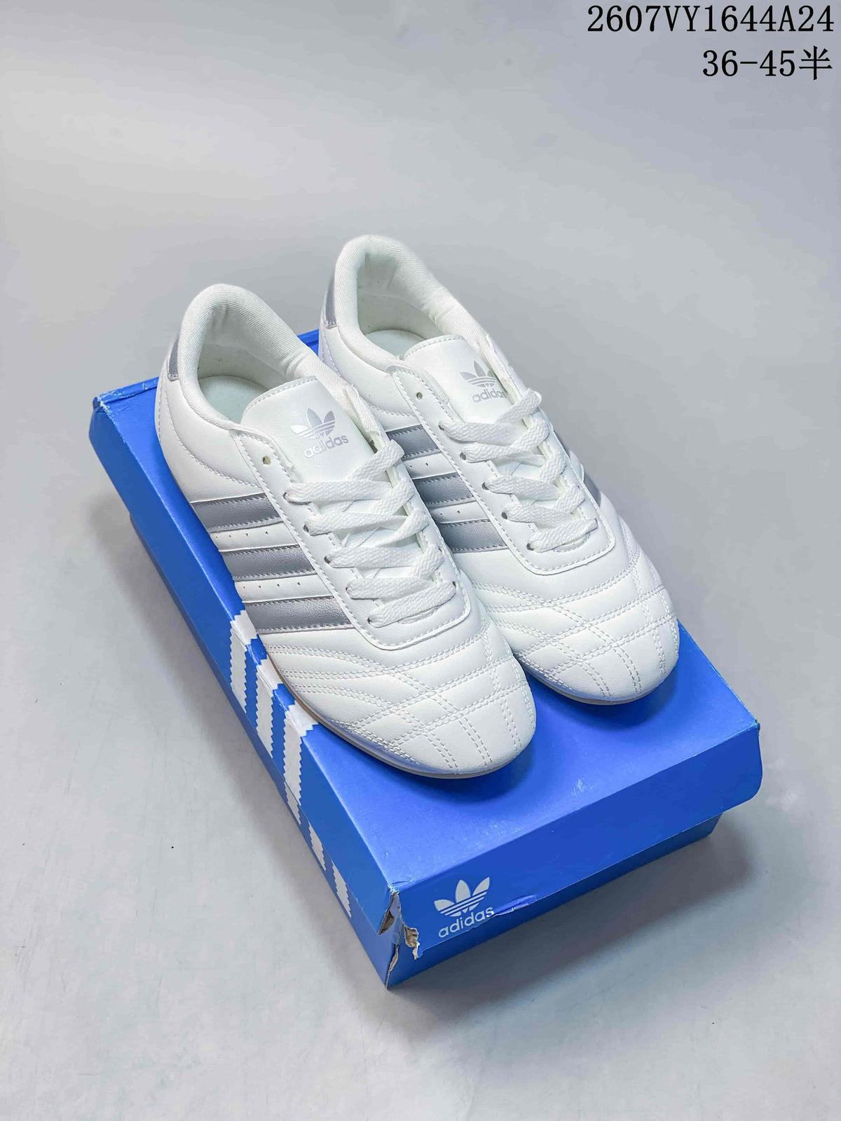 Pair of white and silver adidas Taekwondo sneakers displayed on a blue shoebox.