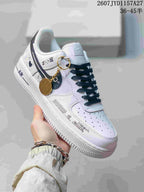 Angled side view of a white and black Nike Air Force 1 ’07 sneaker with graphic side detailing and a gold-tone decorative charm.