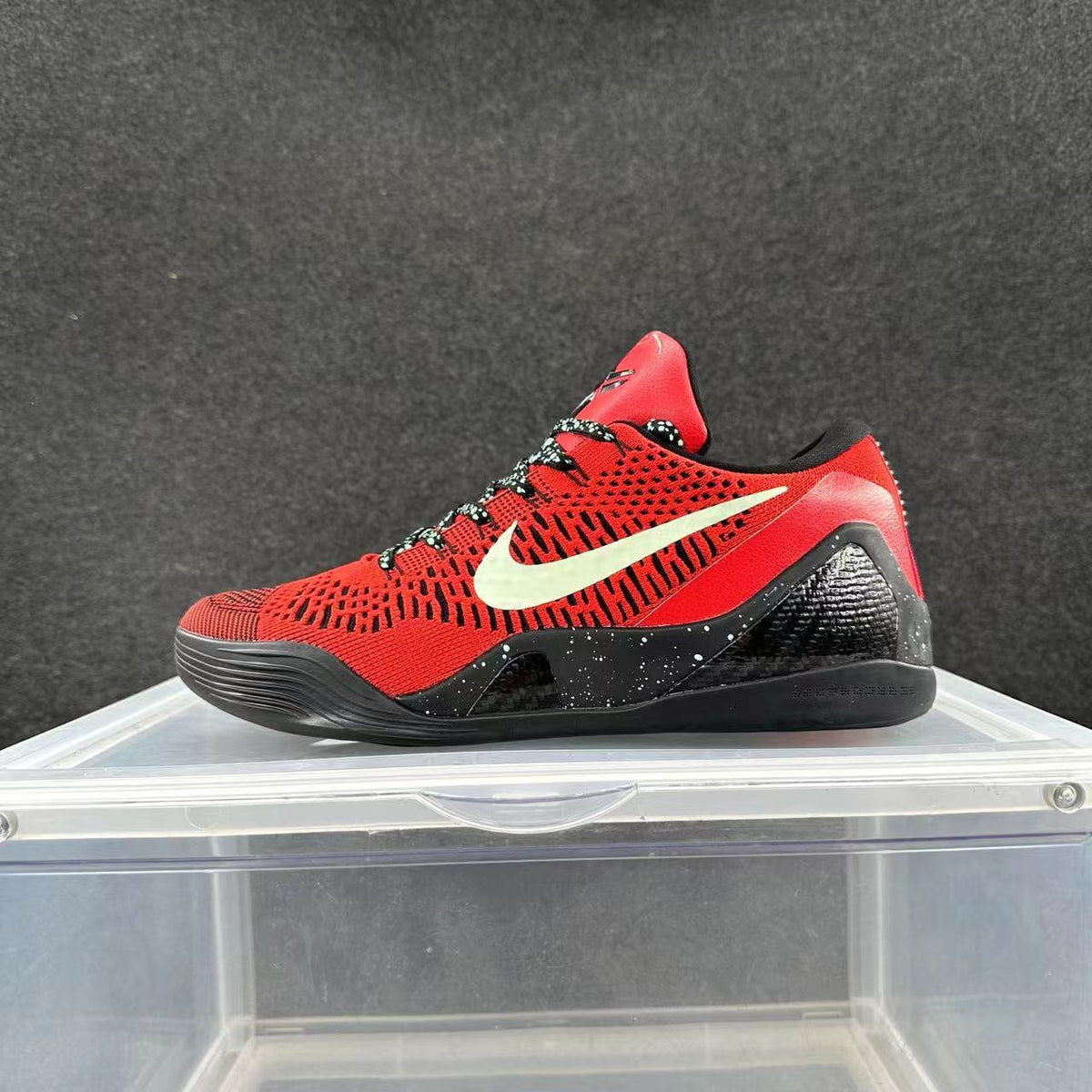 Red and black Nike basketball sneaker displayed in side profile on a clear stand.