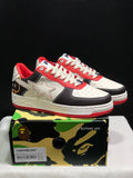 Pair of BAPE STA low-top sneakers in white, black, and red displayed above a branded camouflage shoe box; the box label shows EUR 41 and CM 26 for the photographed sample.