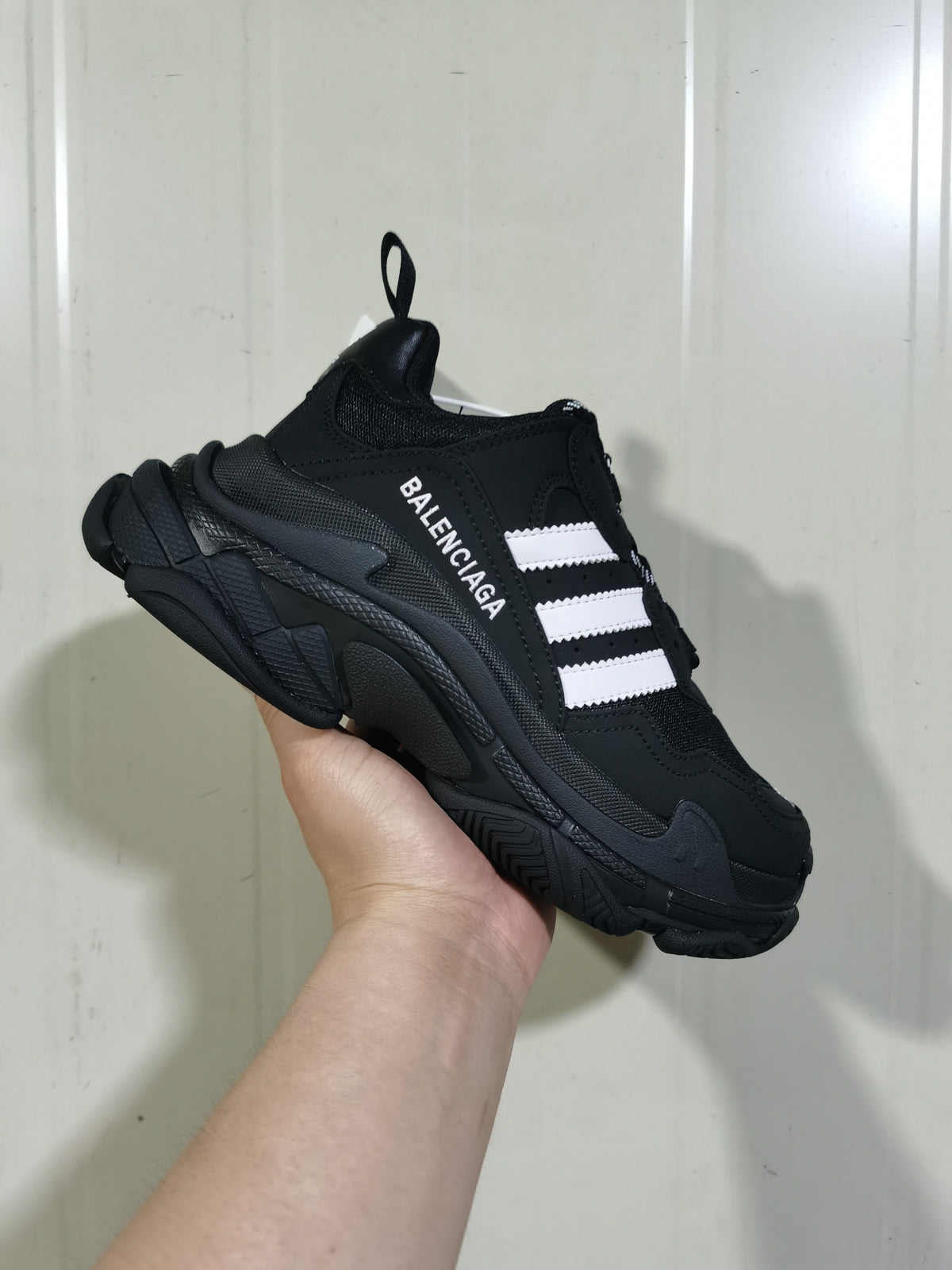 Angled view of a black and white Balenciaga Triple S sneaker showing the white side stripes, layered upper, chunky sole, and rear pull loop.