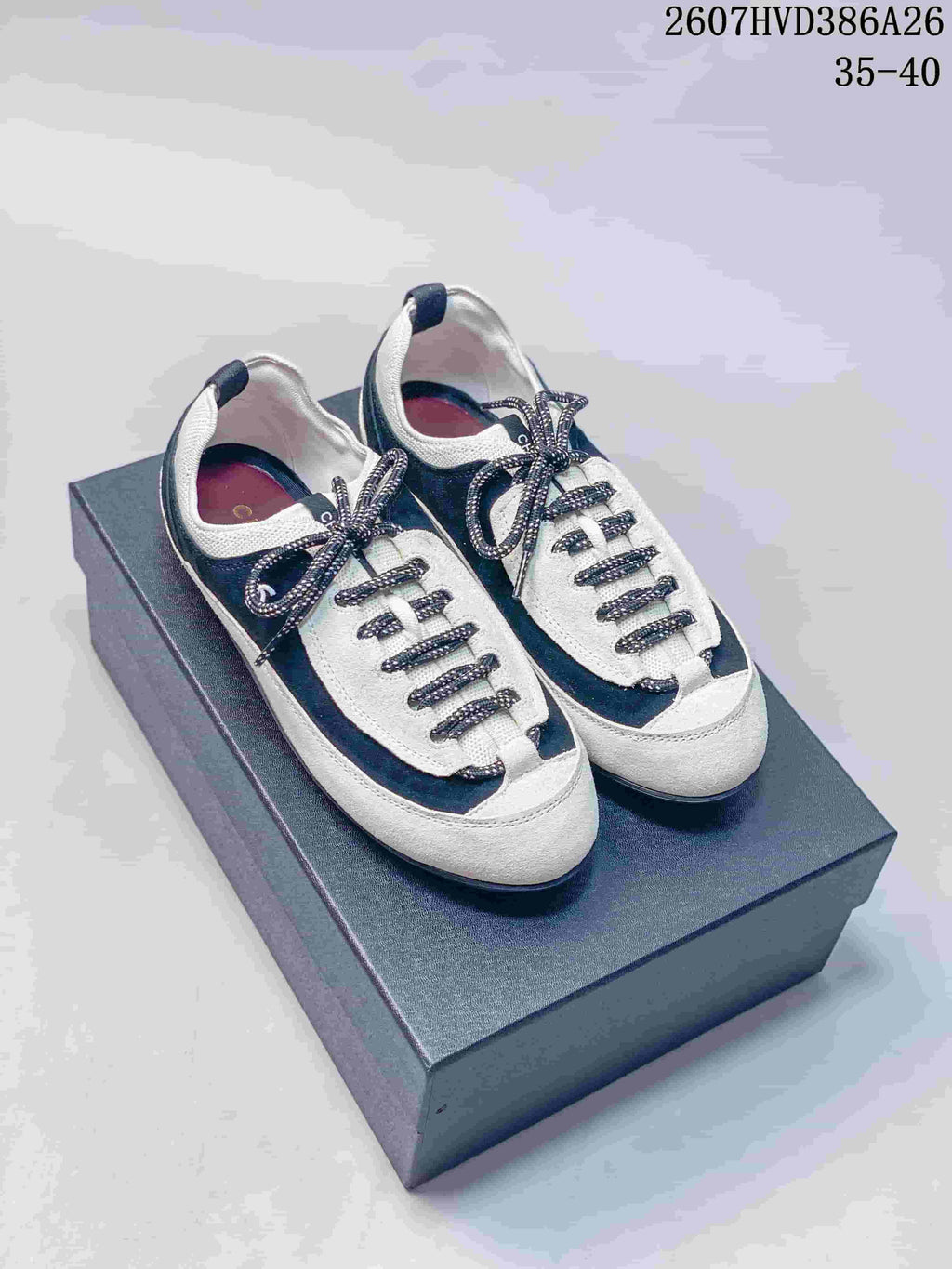 Pair of black-and-white Chanel low-top sneakers displayed on a box, with patterned laces and rounded toes.