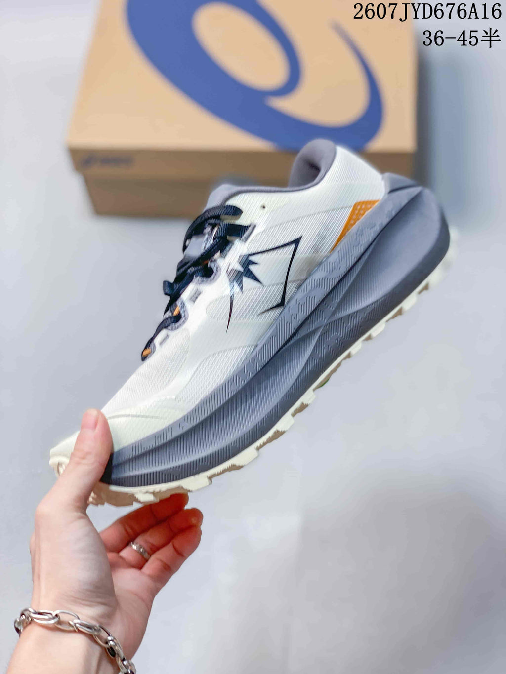 Side view highlighting the white upper, dark ASICS branding, gray midsole, orange heel accent, and trail-style outsole.
