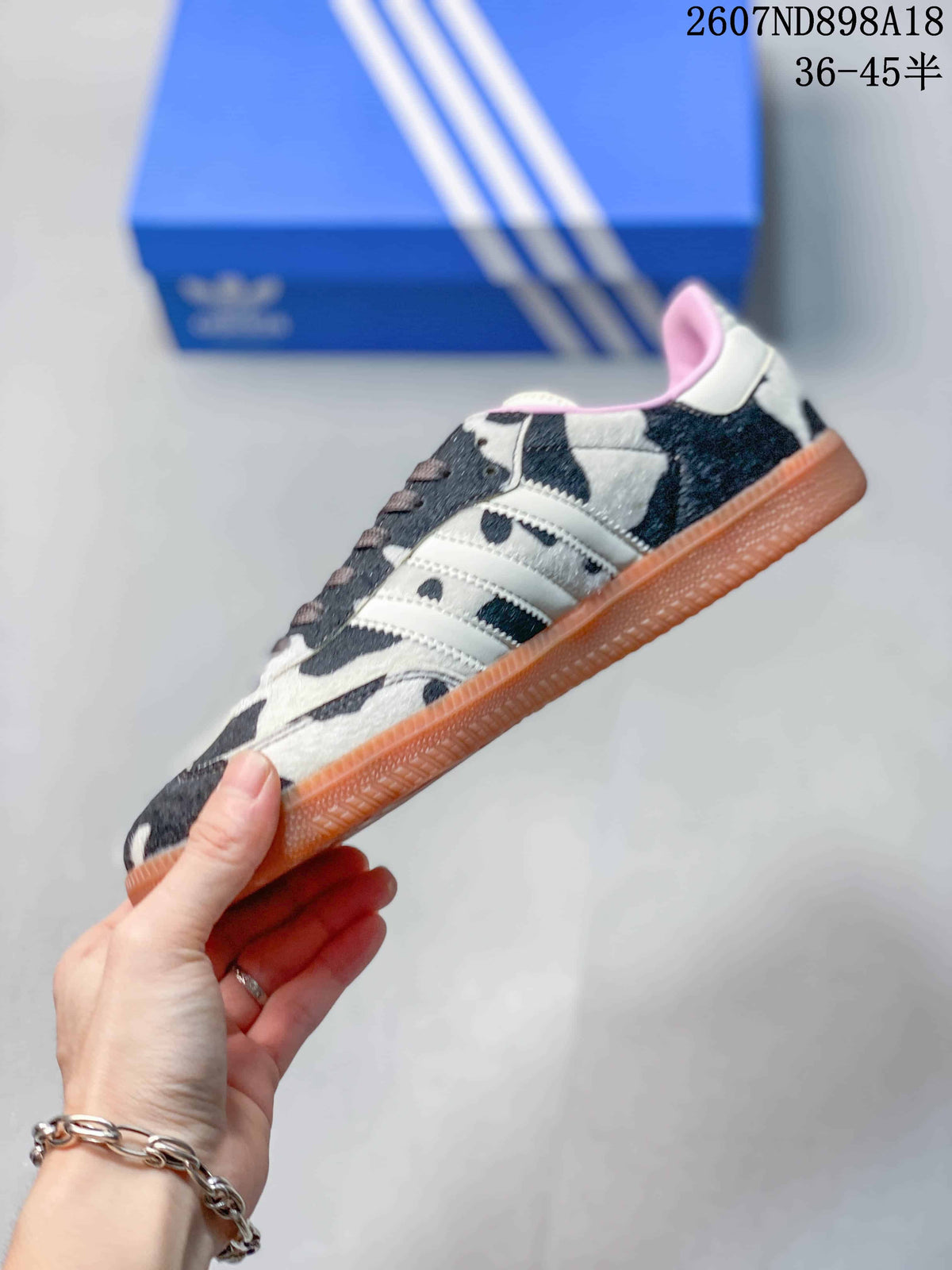 Side profile showing the cow-print upper, white three stripes, lace-up construction and gum-colored outsole.
