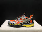 Outer side profile showing the arrow-shaped overlays, orange upper panels, black accents, and yellow midsole area.