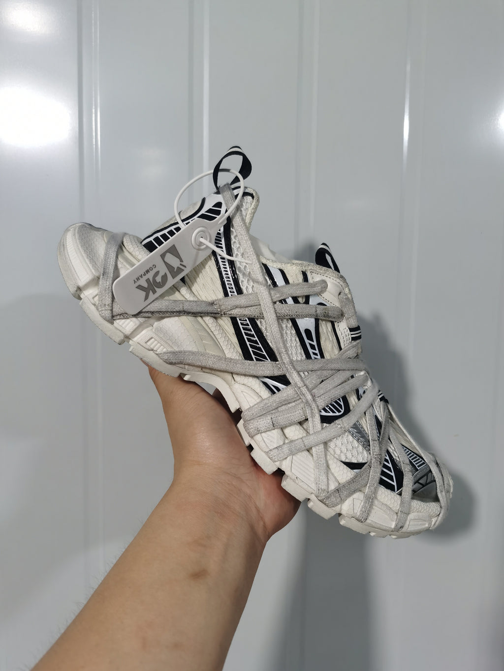 Close-up angled view of a white and black sneaker with layered gray laces and graphic side panels.