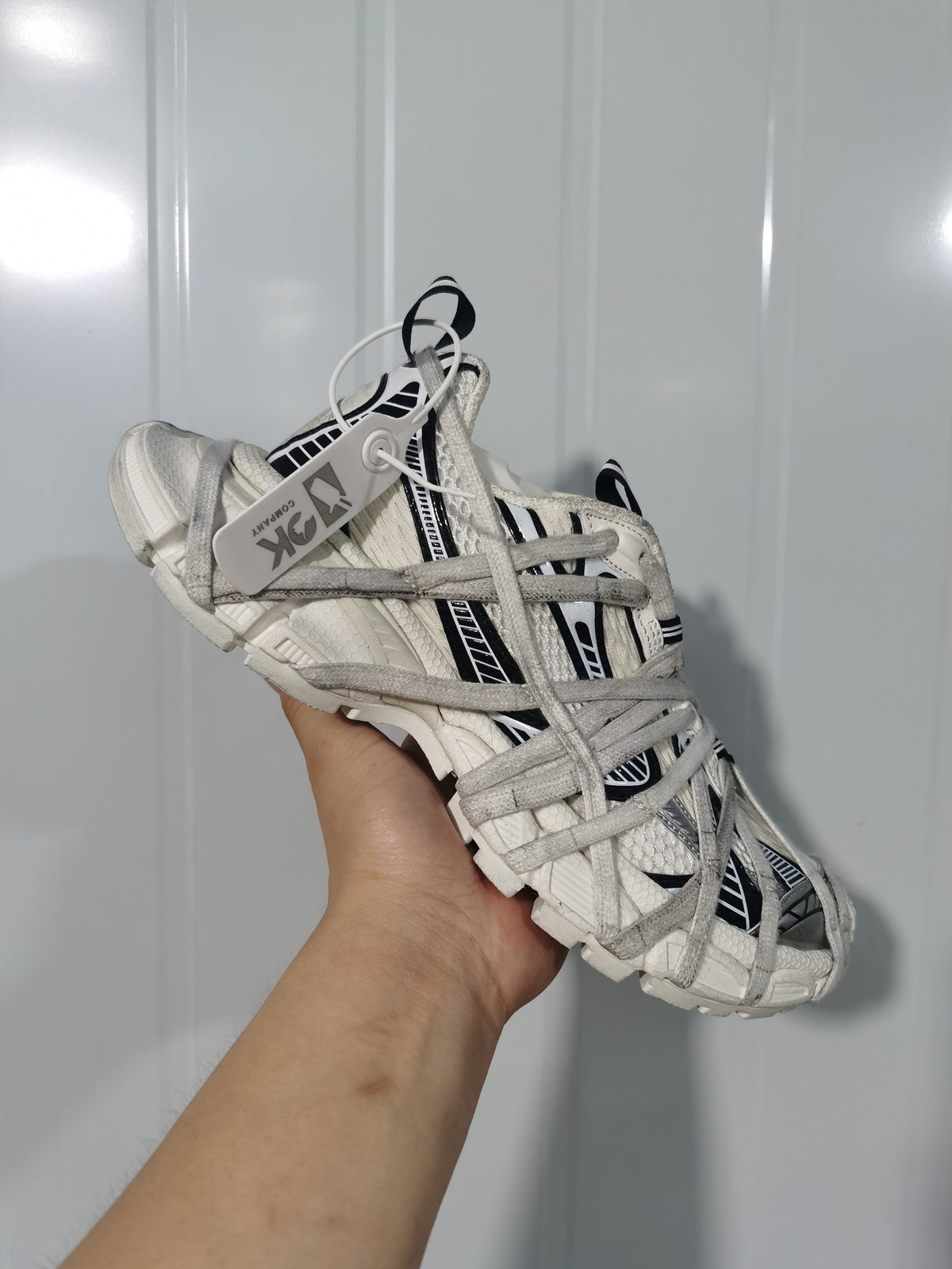 Close-up angled view of a white and black sneaker with layered gray laces and graphic side panels.