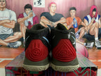 Rear view of dark basketball shoes with red heel pieces, light blue logo details, and a patterned outsole.