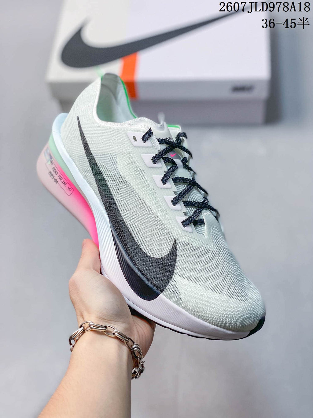 Light-colored Nike racing sneaker with black side branding, dark laces, and pink and mint sole accents; image text shows style code 2607JLD978A18 and size range 36–45.