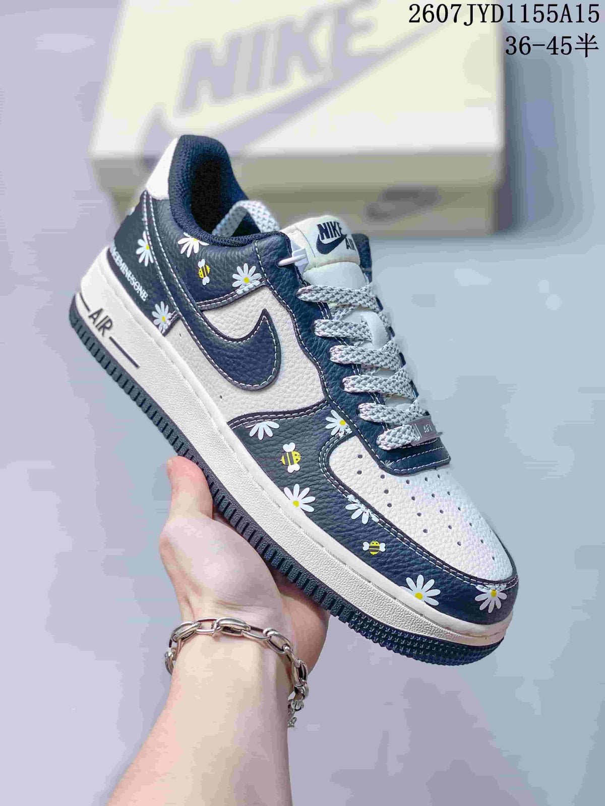 White and navy Nike Air Force 1 sneaker decorated with daisy flowers and bee motifs across the dark panels.