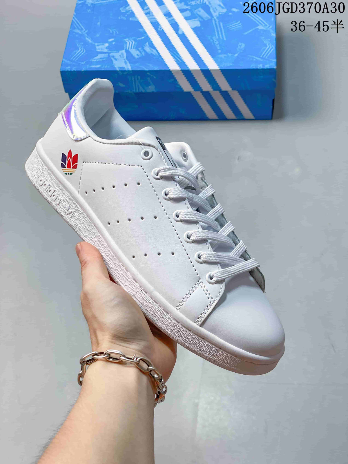 White Stan Smith-style sneaker with a multicolor heel emblem and an iridescent heel tab.