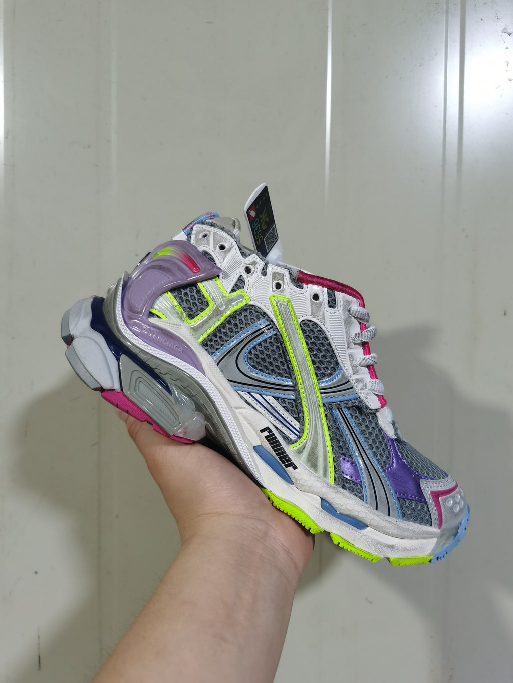 Angled front view of the Balenciaga Runner sneaker showing its grey mesh upper, purple overlays, neon yellow details and multi-color outsole.