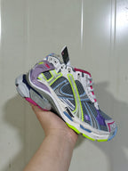 Angled front view of the Balenciaga Runner sneaker showing its grey mesh upper, purple overlays, neon yellow details and multi-color outsole.
