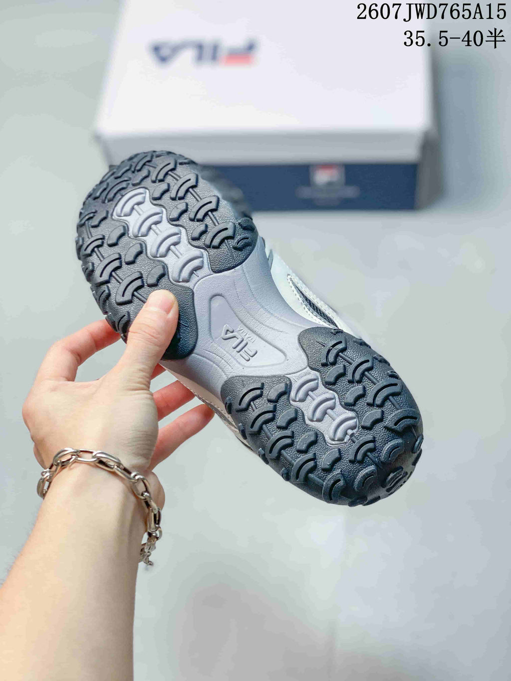 Close-up of the textured black-and-gray outsole on a FILA sneaker; overlay shows style code 2607JWD765A15 and size range 35.5–40.5.