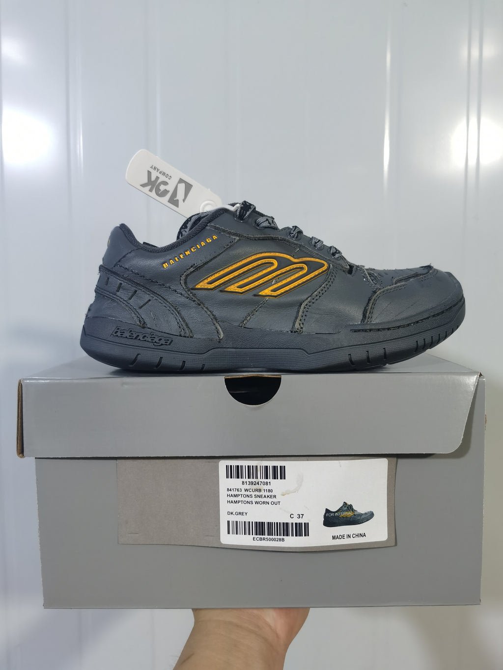Side view of the dark grey Hampton sneaker placed on its box, with the product label visible below.