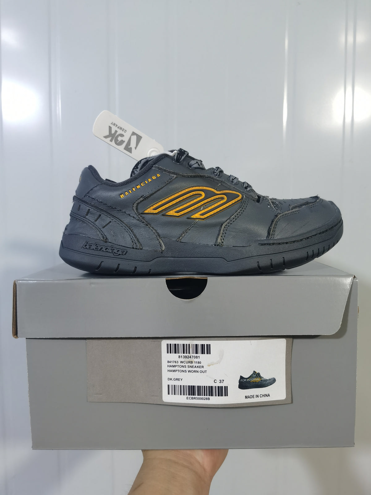 Side view of the dark grey Hampton sneaker placed on its box, with the product label visible below.