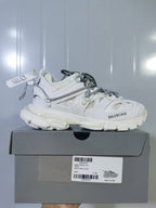 Side profile of the white sneaker resting on a gray box, with a visible label reading Track Trail Laces, White, and C 39.