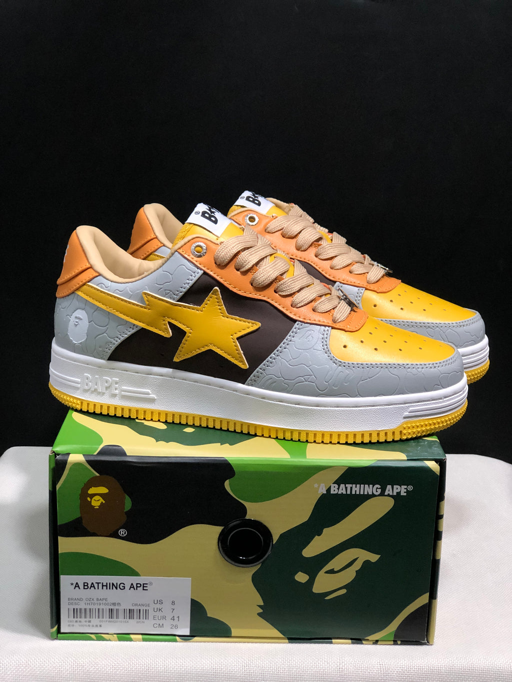 Pair of grey and yellow BAPE STA low-top sneakers displayed on a branded shoebox.