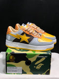 Pair of grey and yellow BAPE STA low-top sneakers displayed on a branded shoebox.
