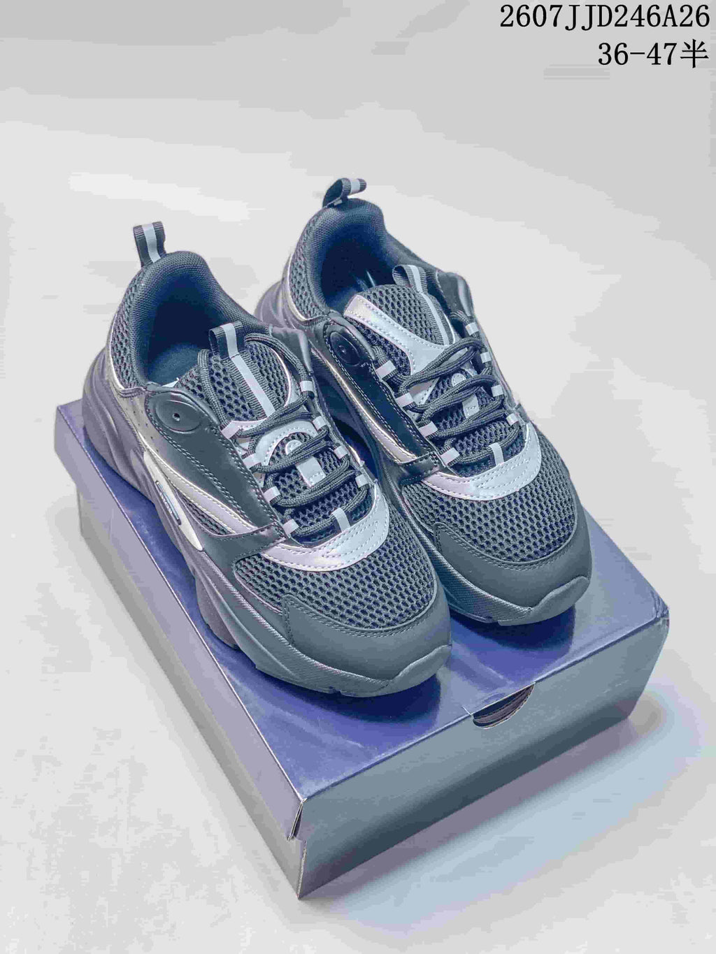 Pair of dark gray and black Dior low-top sneakers with silver-gray accents displayed on a shoebox.