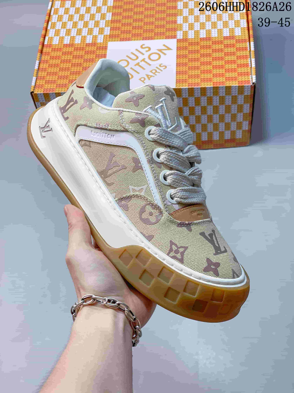 Angled close-up of a beige monogram-patterned low-top sneaker with white laces, white side trim, and a gum-colored sole.