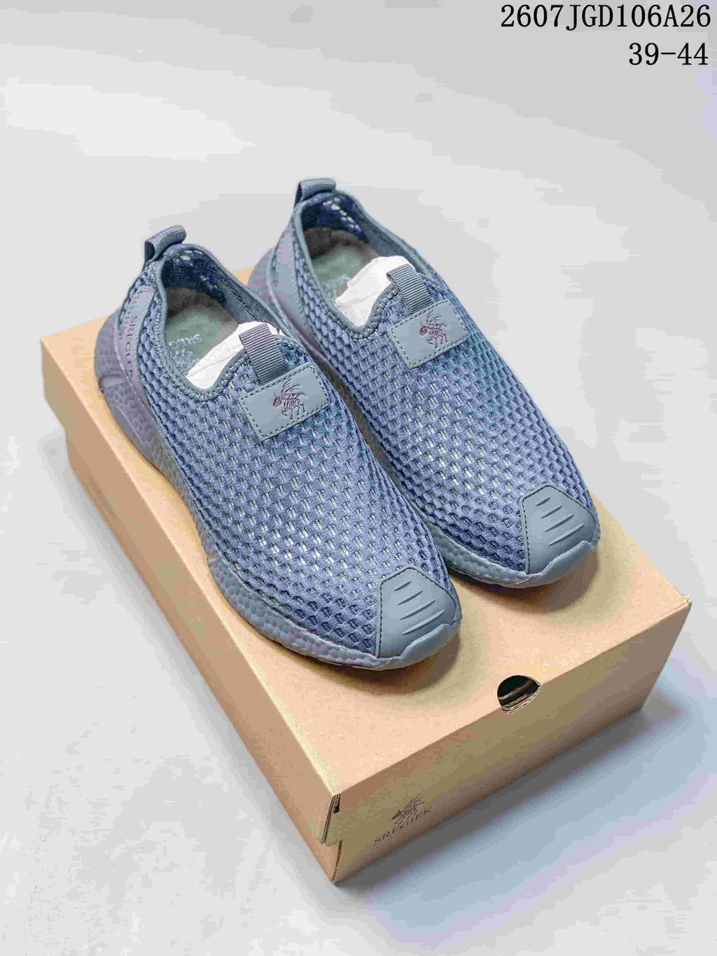 Pair of blue-gray SREGIEK slip-on sneakers displayed on a shoebox, showing the mesh upper, toe overlays, pull tabs, and thick sole.