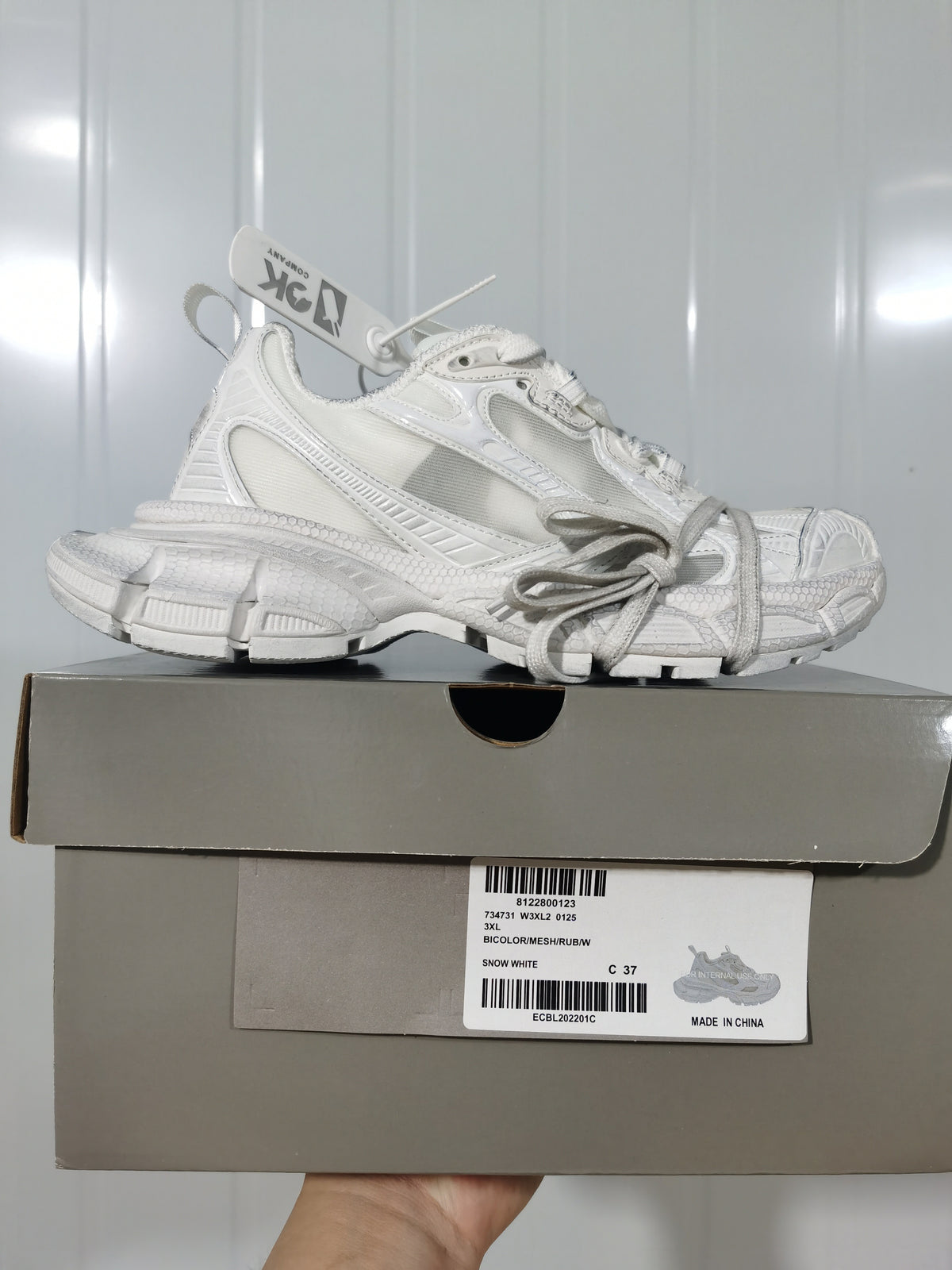 Side profile of the snow white sneaker resting on its box; the label shows style information, color "SNOW WHITE," and size C 37.