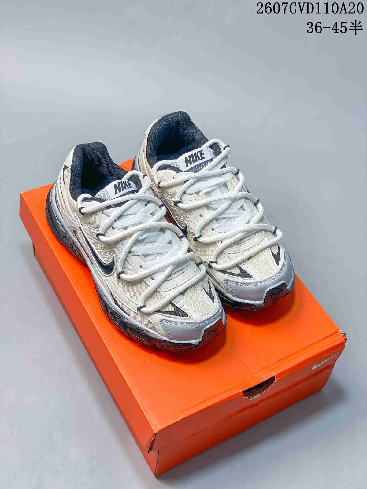 Pair of Nike Initiator sneakers in grey and white displayed on an orange shoebox; style code 2607GVD110A20 and size range 36–45.5 are visible at the top.