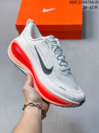 White Nike Vomero Plus running shoe shown from the side with a bright red-orange heel and midsole accent.