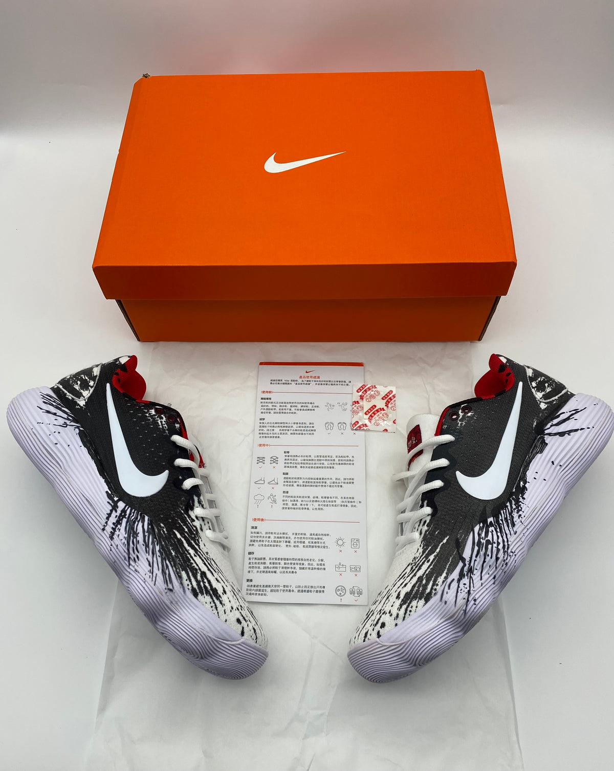 Pair of black-and-white graphic Nike shoes pictured with an orange Nike box and printed insert.