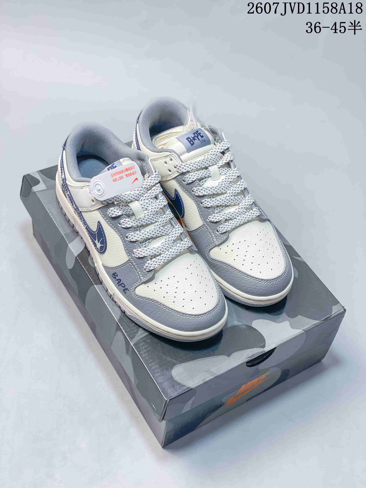 Pair of cream, gray, and blue Nike SB Dunk Low sneakers displayed on a patterned shoe box.