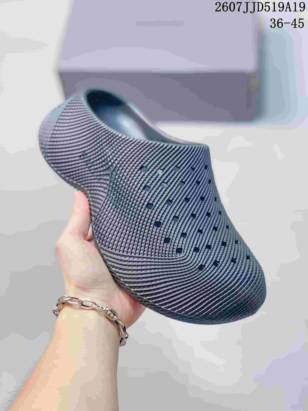 Angled side view of a gray perforated slip-on clog highlighting the textured pattern, open heel, and raised sole.