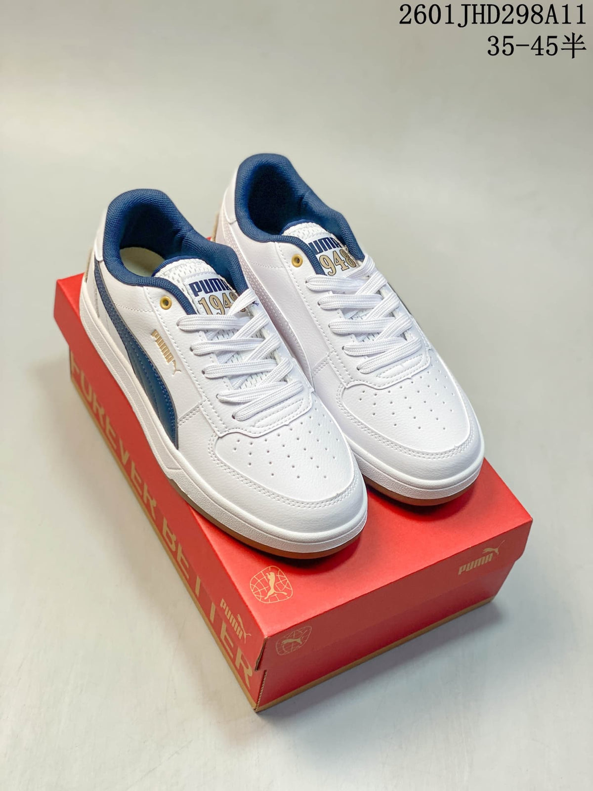 Pair of white and navy Puma Caven 2.0 sneakers displayed on a red Puma shoebox.