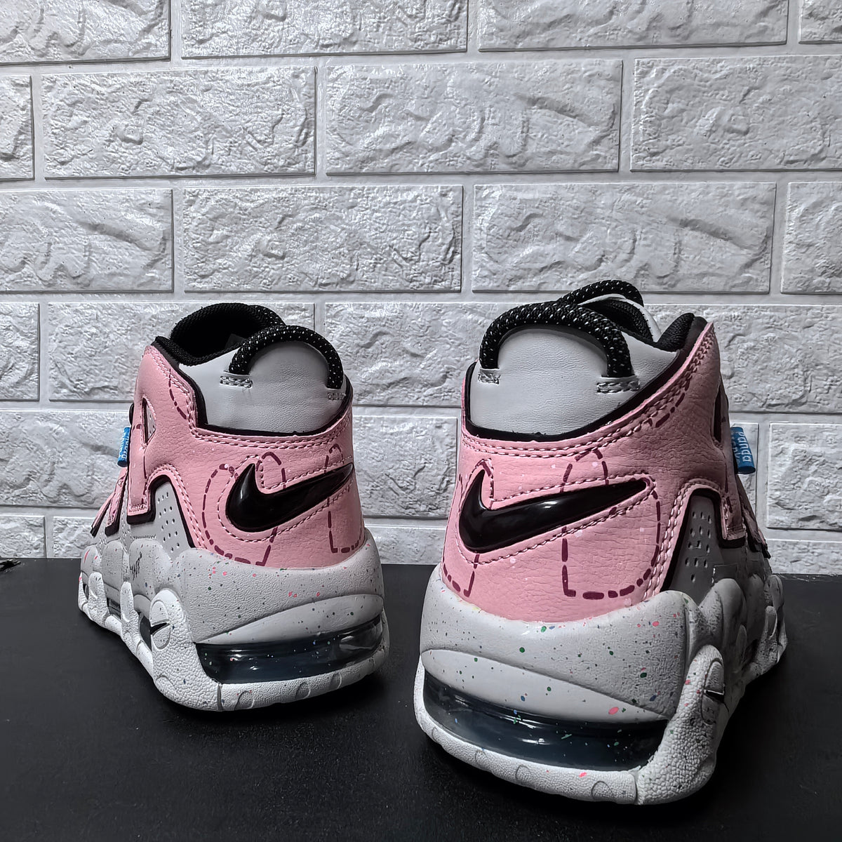 Rear view of pink and grey Nike sneakers with black Swoosh details and heel cushioning windows