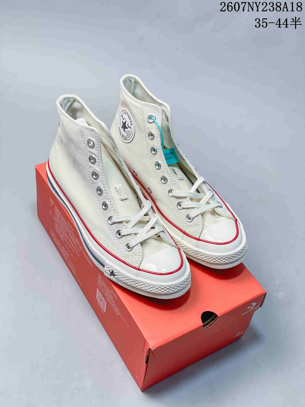 Pair of off-white Converse high-top sneakers displayed on a red shoebox, showing the side patches, red and blue midsole stripes, and lace-up fronts.