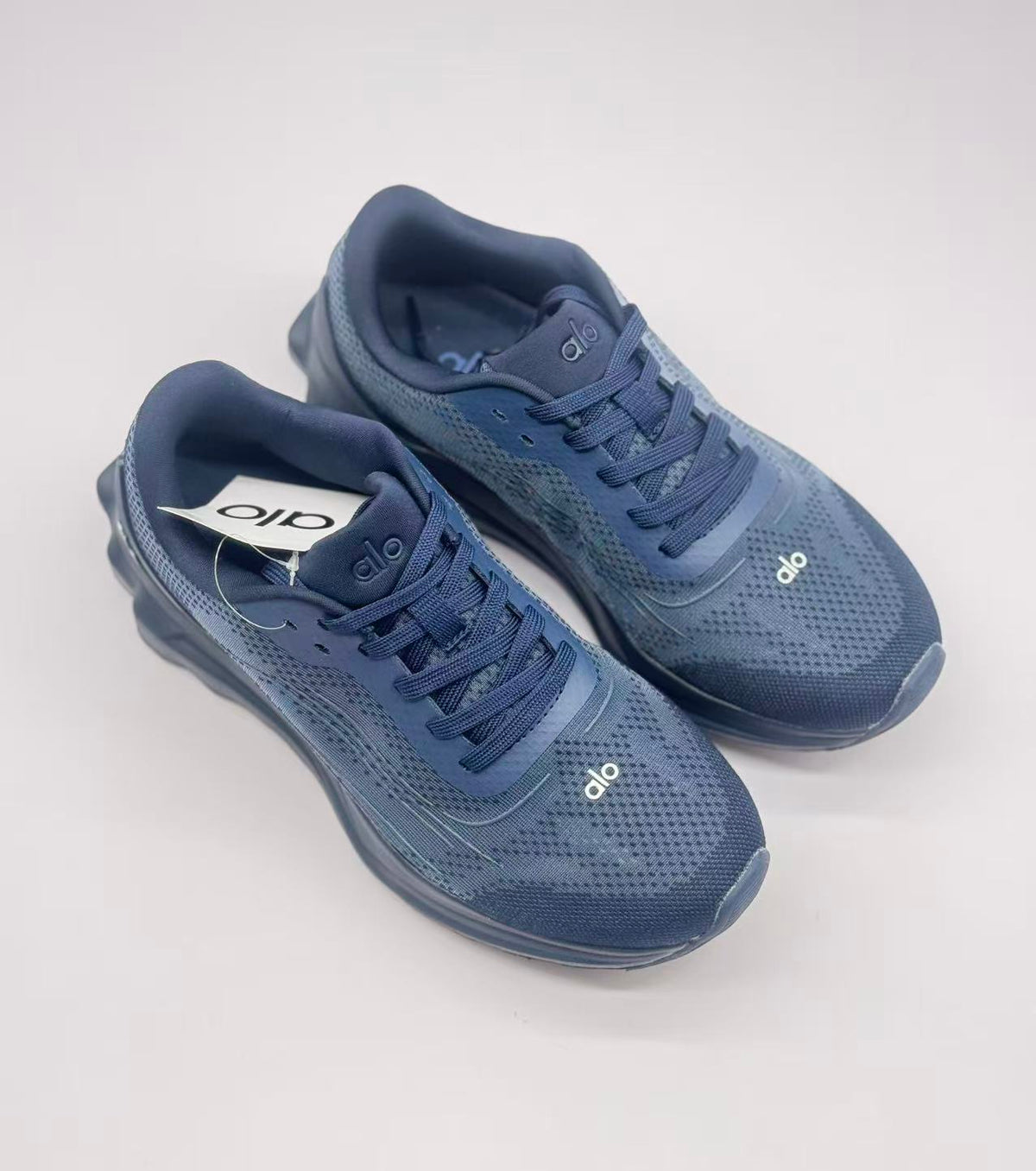 Top-down view of the dark blue Alo sneaker pair showing the laces, padded collars, and patterned uppers.