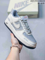 Close-up side view of a white and grey patterned sneaker with visible side graphics, perforated toe box, and Air sole branding.
