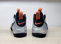 Rear view of silver and black Nike Air Foamposite Pro sneakers with orange pull tabs and accents