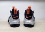 Rear view of silver and black Nike Air Foamposite Pro sneakers with orange pull tabs and accents