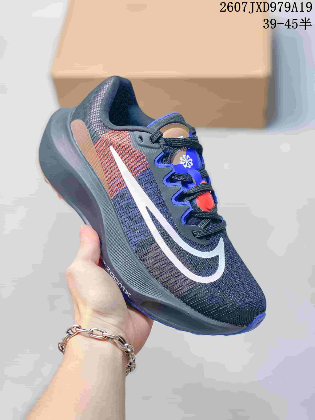 Angled side view showing the dark charcoal upper, white swoosh, tan and red side accents and blue outsole details.