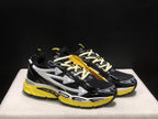 Three-quarter front view of the black sneakers with white arrow graphics, light laces, and yellow soles.